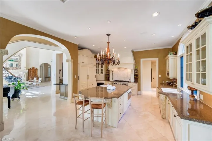 Kitchen with glass fronted cabinets, arched walkways, dark stone counters, a kitchen island, and suspended lighting