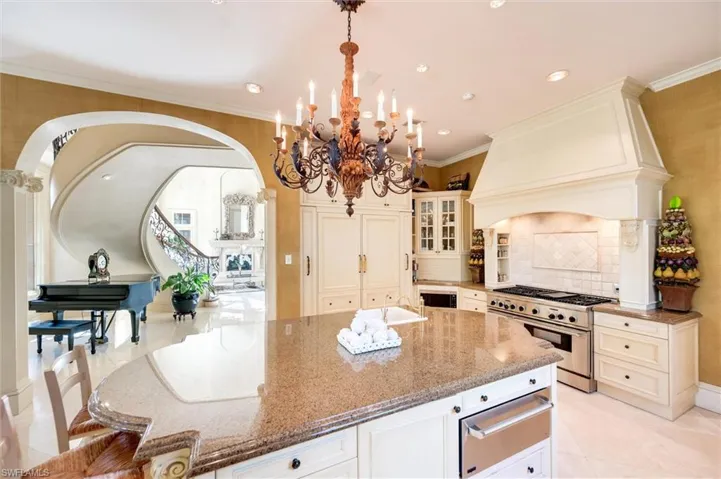 Kitchen with light stone counters, glass fronted cabinets, a warming drawer, stainless steel stove, and tasteful backsplash