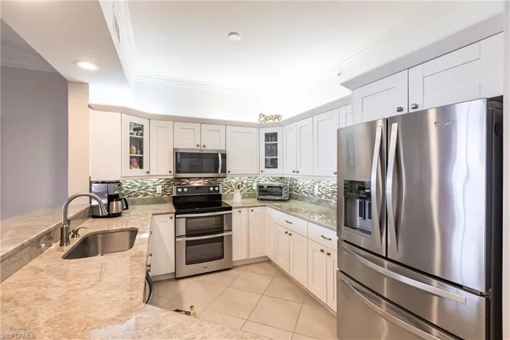 Kitchen with appliances with stainless steel finishes, ornamental molding, white cabinetry, light stone counters, and light tile patterned floors