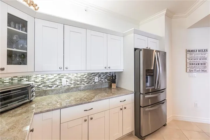 Kitchen with stainless steel fridge with ice dispenser, crown molding, white cabinetry, glass insert cabinets, and light tile patterned floors