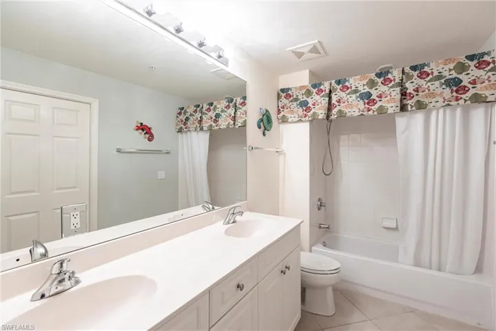 Bathroom featuring shower / bathtub combination with curtain, light tile patterned floors, and double vanity