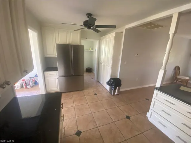 Kitchen featuring tile flooring with decorative accents, white cabinetry, dark countertops, and a ceiling fan