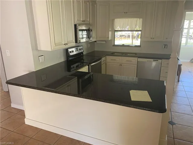 Kitchen featuring a U-shaped countertop with a breakfast bar extension, white shaker-style cabinetry, dark stone countertops, stainless steel appliances, and tile flooring