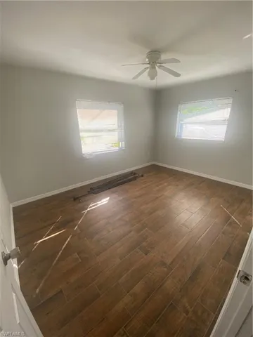 Spacious room featuring wood-finish plank flooring, two windows, and a ceiling fan with integrated lighting