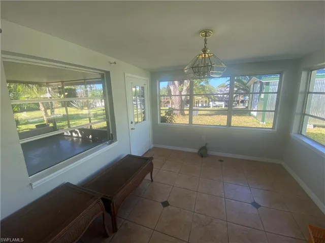 Sunroom featuring expansive windows, tile flooring with decorative inserts, a glass-paneled entry door, and a central ceiling light fixture