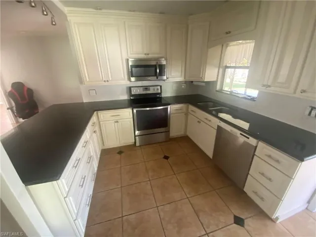 U-shaped kitchen featuring white cabinetry, dark countertops, stainless steel appliances, a double basin sink, and tile flooring