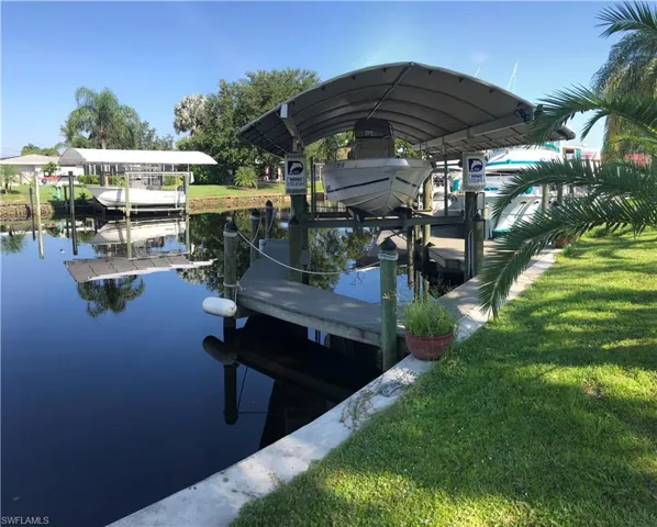Waterfront property featuring a covered boat lift, concrete dock, and manicured lawn