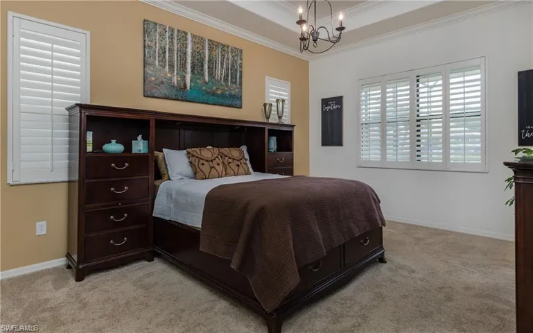 Bedroom featuring ornamental molding, a chandelier, light carpet, and a tray ceiling