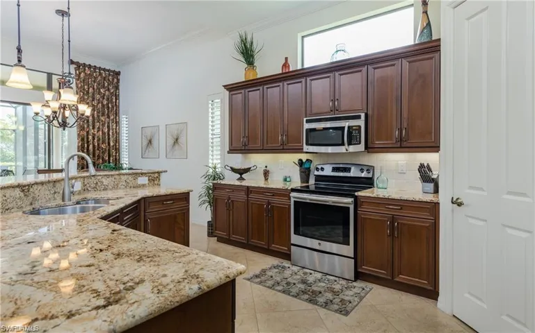 Kitchen featuring dark brown cabinets, appliances with stainless steel finishes, tasteful backsplash, light stone counters, and crown molding