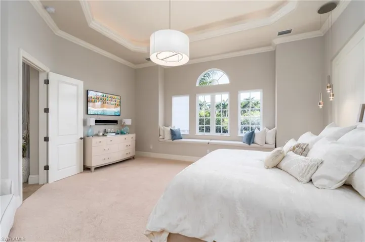 Bedroom with a tray ceiling, light carpet, and ornamental molding