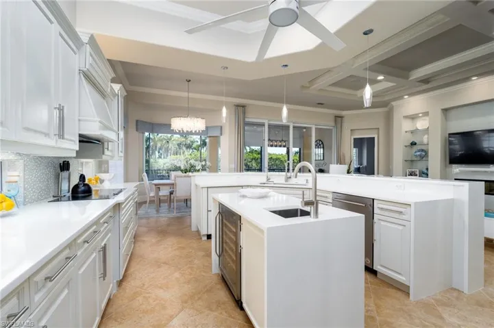 Kitchen featuring crown molding, hanging light fixtures, light stone counters, beverage cooler, and coffered ceiling