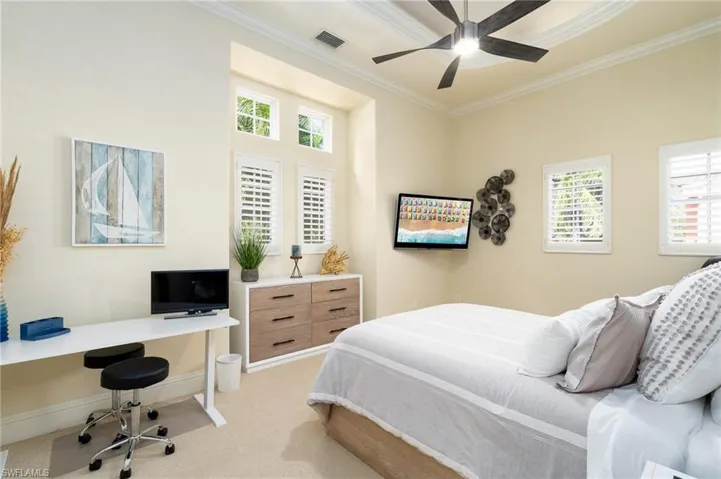 Bedroom with ornamental molding, light colored carpet, a desk, and a ceiling fan