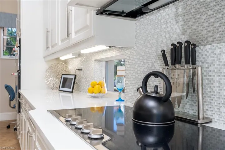 Kitchen featuring white cabinets, range hood, and light stone countertops