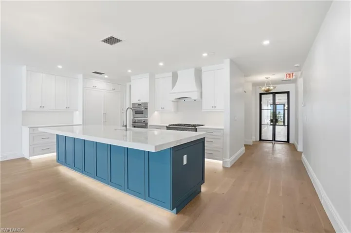 Two tone kitchen with dual tone cabinets, an island with sink, light wood-style flooring, light stone countertops, and recessed lighting