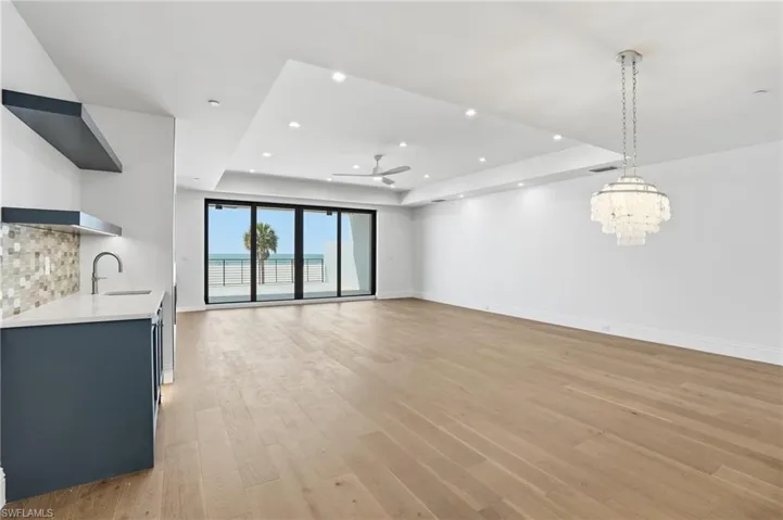 Unfurnished living room featuring light wood-type flooring, a ceiling fan, a raised ceiling, and suspended lighting