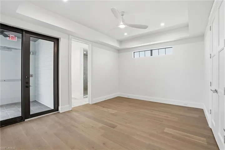 Unfurnished bedroom featuring a raised ceiling, ceiling fan, recessed lighting, light wood finished floors, and ensuite bathroom