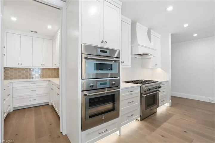 Kitchen with stainless steel appliances, white cabinetry, recessed lighting, light wood-style floors, and light stone counters