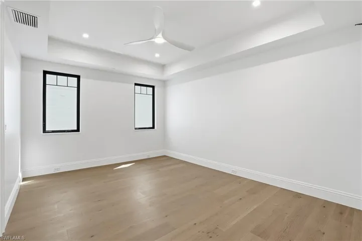 Empty room featuring a raised ceiling, ceiling fan, light wood finished floors, and recessed lighting