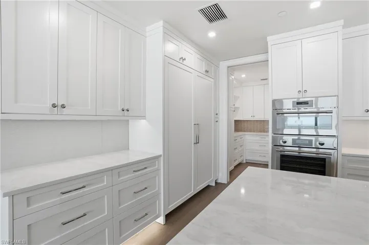 Kitchen with white cabinetry, double oven, light stone countertops, decorative backsplash, and recessed lighting