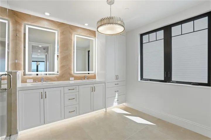 Bathroom with double vanity, light tile patterned floors, and a shower stall
