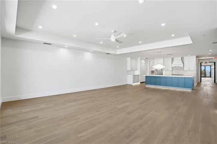 Unfurnished living room with a tray ceiling, a ceiling fan, light wood-type flooring, and recessed lighting