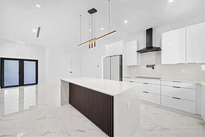 Kitchen with white cabinets, decorative light fixtures, light marble finish floors, and modern cabinets