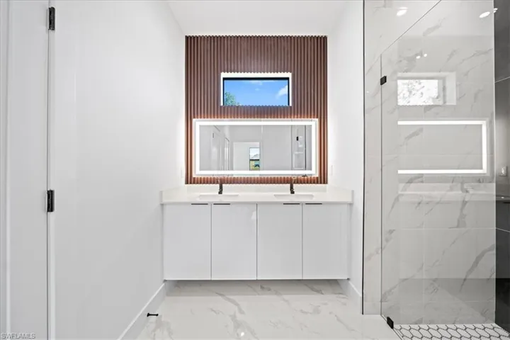 Bathroom featuring double vanity, a marble finish shower, and light marble finish floors