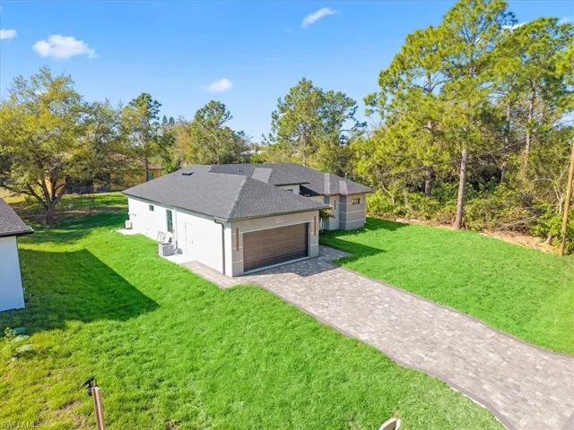View of front of home with a front yard, roof with shingles, a garage, decorative driveway, and stucco siding