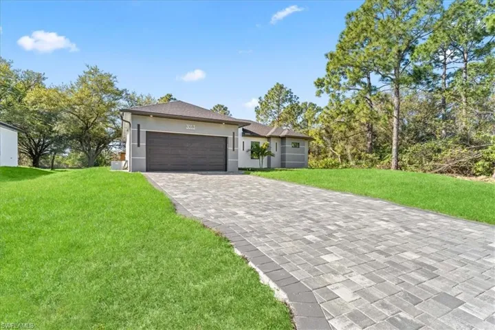 View of front of home with a front yard, decorative driveway, stucco siding, and a garage