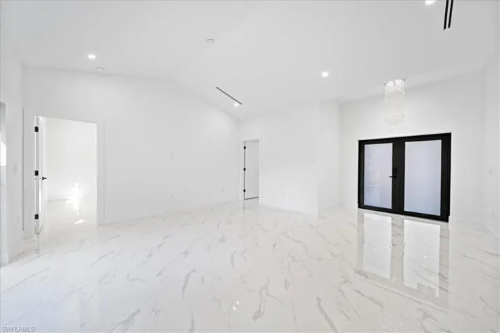 Spare room featuring french doors, vaulted ceiling, recessed lighting, and light marble finish flooring