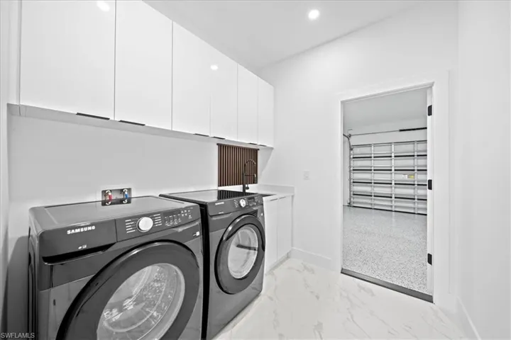 Laundry room featuring light marble finish flooring, separate washer and dryer, cabinet space, and recessed lighting