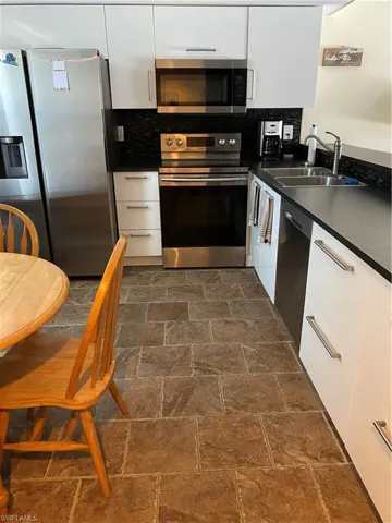Kitchen featuring appliances with stainless steel finishes, dark countertops, white cabinetry, backsplash, and modern cabinets