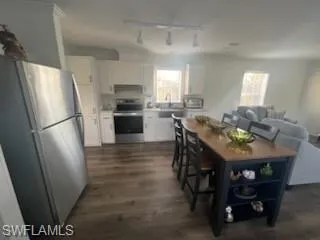 Kitchen with stainless steel appliances, white cabinetry, track lighting, dark wood-type flooring, and light countertops
