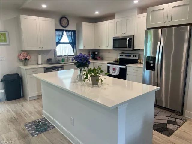 Kitchen with white cabinets, stainless steel appliances, light hardwood / wood-style flooring, and a center island