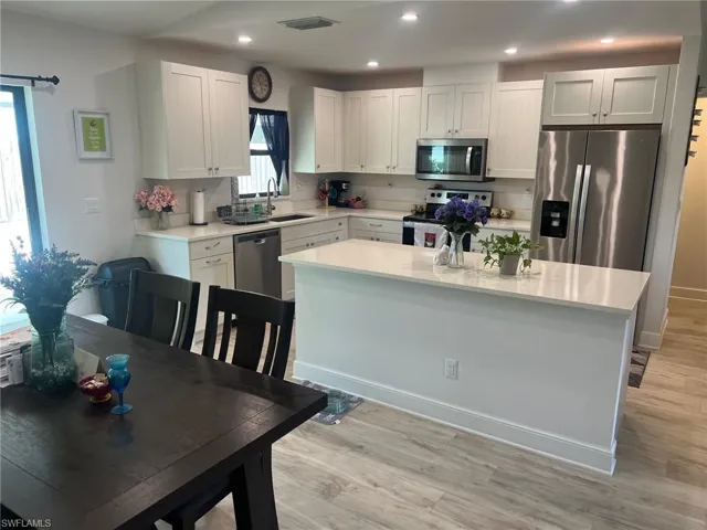 Kitchen with white cabinetry, a center island, stainless steel appliances, light hardwood / wood-style floors, and sink