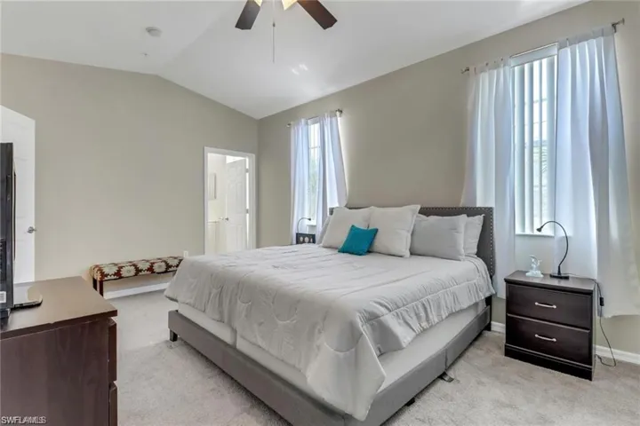 Bedroom featuring light carpet, baseboards, connected bathroom, a ceiling fan, and lofted ceiling