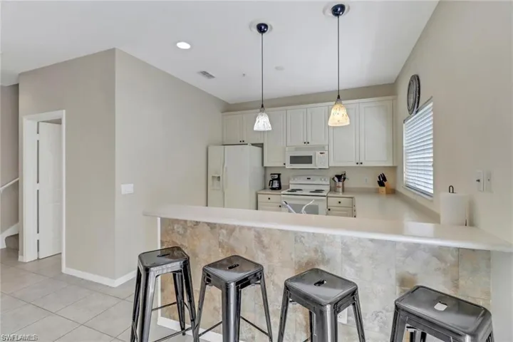 Kitchen featuring a breakfast bar area, a peninsula, white appliances, visible vents, and light countertops