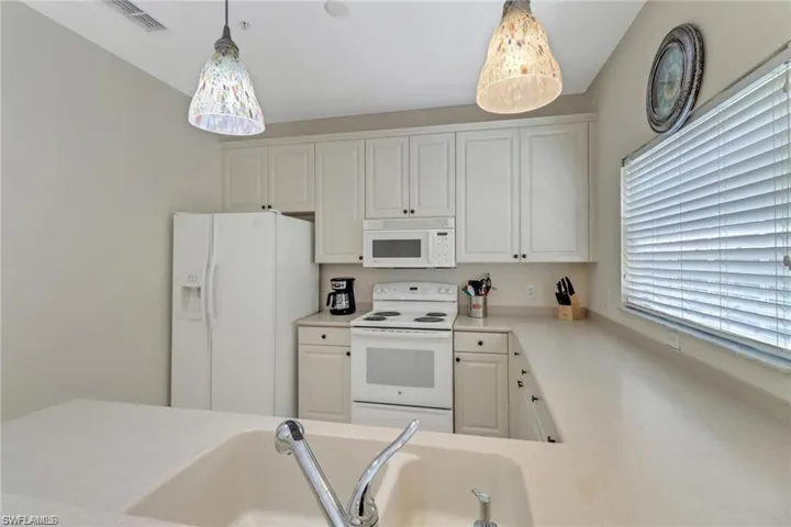 Kitchen with white appliances, visible vents, white cabinets, light countertops, and hanging light fixtures
