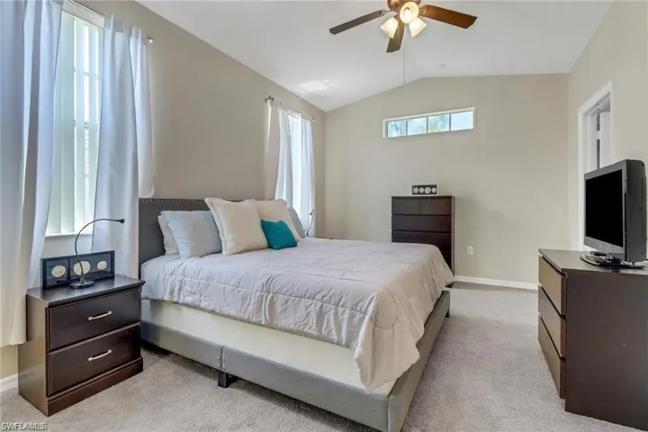 Bedroom with lofted ceiling, ceiling fan, light carpet, and baseboards