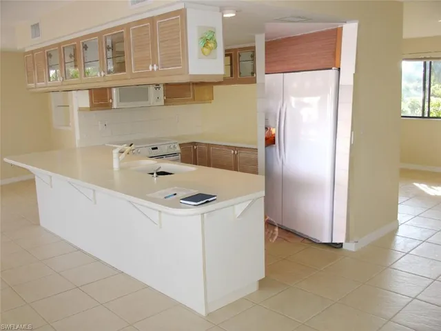 Kitchen with white appliances, sink, decorative backsplash, light tile patterned floors, and kitchen peninsula, breakfast bar
