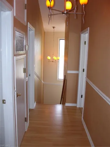 Hallway featuring light hardwood / wood-style floors and a notable chandelier Halway upstairs to stairs downstairs