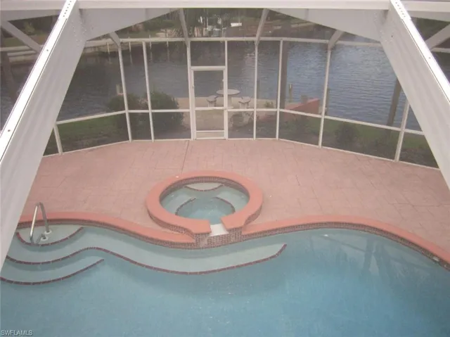 View of swimming pool featuring screen enclosure, an an ground hot tub, a water view, and a patio plus boat dock with beautifull water and intersection canal view