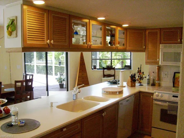 Kitchen with a healthy amount of sunlight, real wood doors, white appliances, and sink