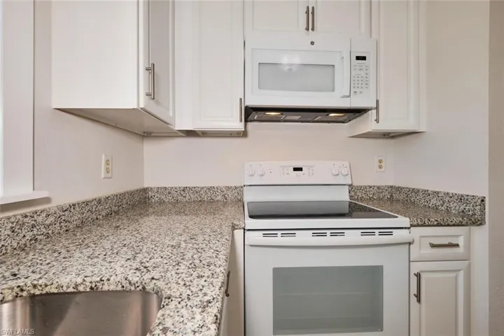 Kitchen featuring white cabinetry, light stone counters, and white appliances