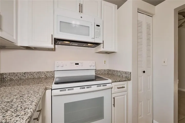 Kitchen with white cabinetry, white appliances, and light stone counters