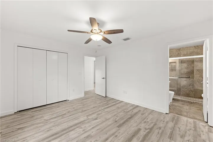 Unfurnished bedroom featuring light wood-type flooring, a ceiling fan, a closet, and ensuite bath