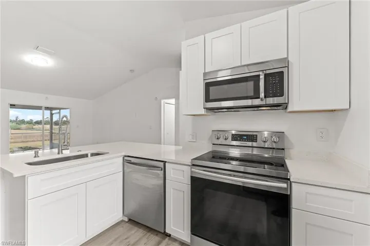 Kitchen with stainless steel appliances, a peninsula, vaulted ceiling, white cabinetry, and light stone counters