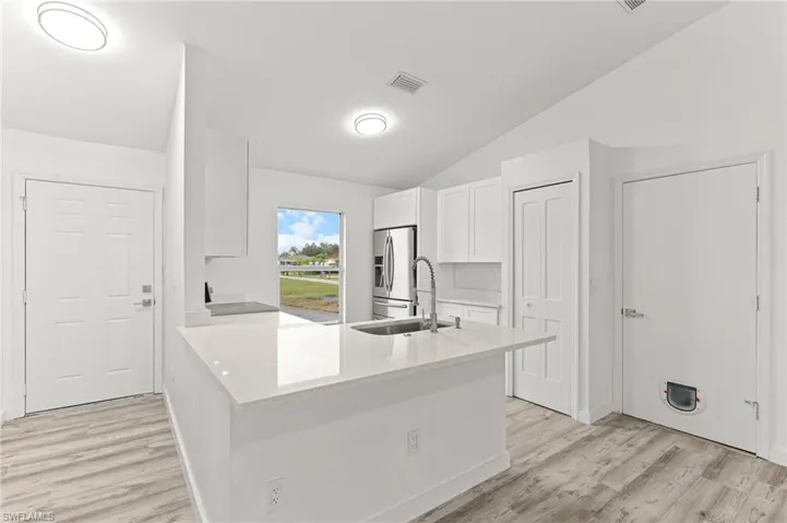 Kitchen with white cabinetry, light stone countertops, stainless steel fridge, light wood-type flooring, and a peninsula