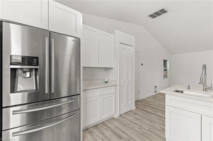 Kitchen with stainless steel fridge with ice dispenser, white cabinets, light stone countertops, vaulted ceiling, and light wood-style flooring