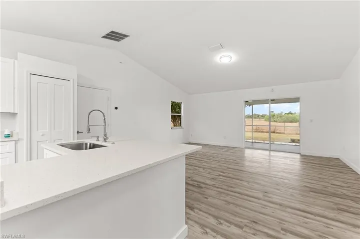 Kitchen with light stone counters, white cabinetry, open floor plan, lofted ceiling, and light wood-style floors
